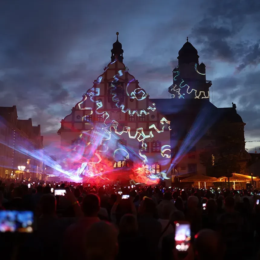 A projection of gears on the facade and a laser show is watched by a crowd
