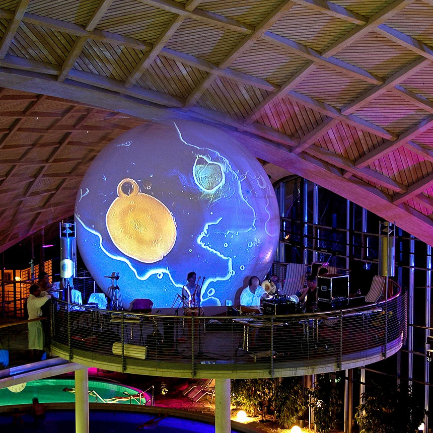 A small orchestra plays on a pedestal, while a round, analog projection accompanies it in the background