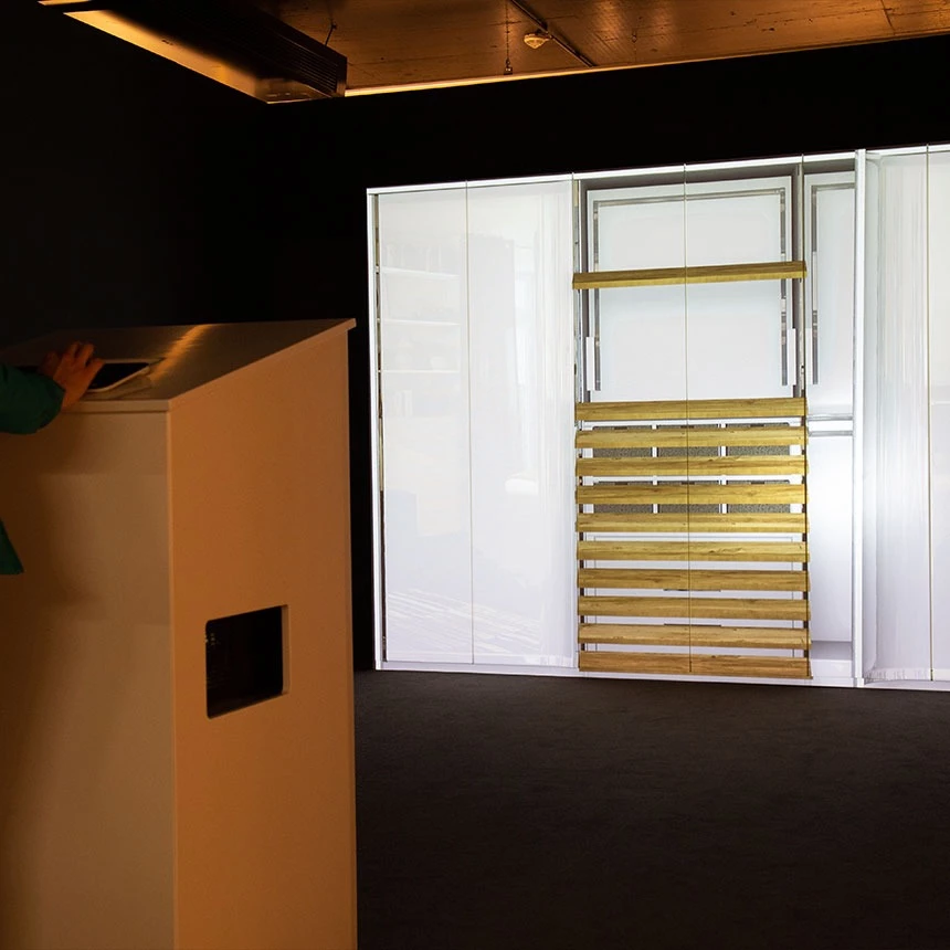 Trade fair visitor stands at stele and uses a tablet that controls the interactive furniture mapping: The projection shows the interior of the cabinet