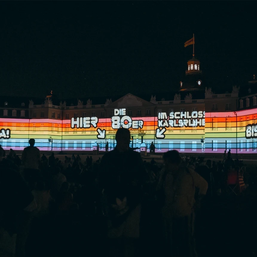 Schlosslichtspiele Karlsruhe: Buntes Retro-Videomapping mit Schriftzug 'Hier 80er im Schloss Karlsruhe' auf der Schlossfassade – Showankündigung und Motto-Clip produziert von TNL GmbH.