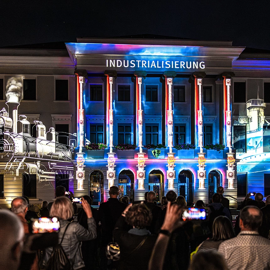 Das Wort "Industrialisierung" steht in der Mitte der Rathausfassade, links ist eine alte Dampflokomotive, rechts ein altes Schiff zu sehen
