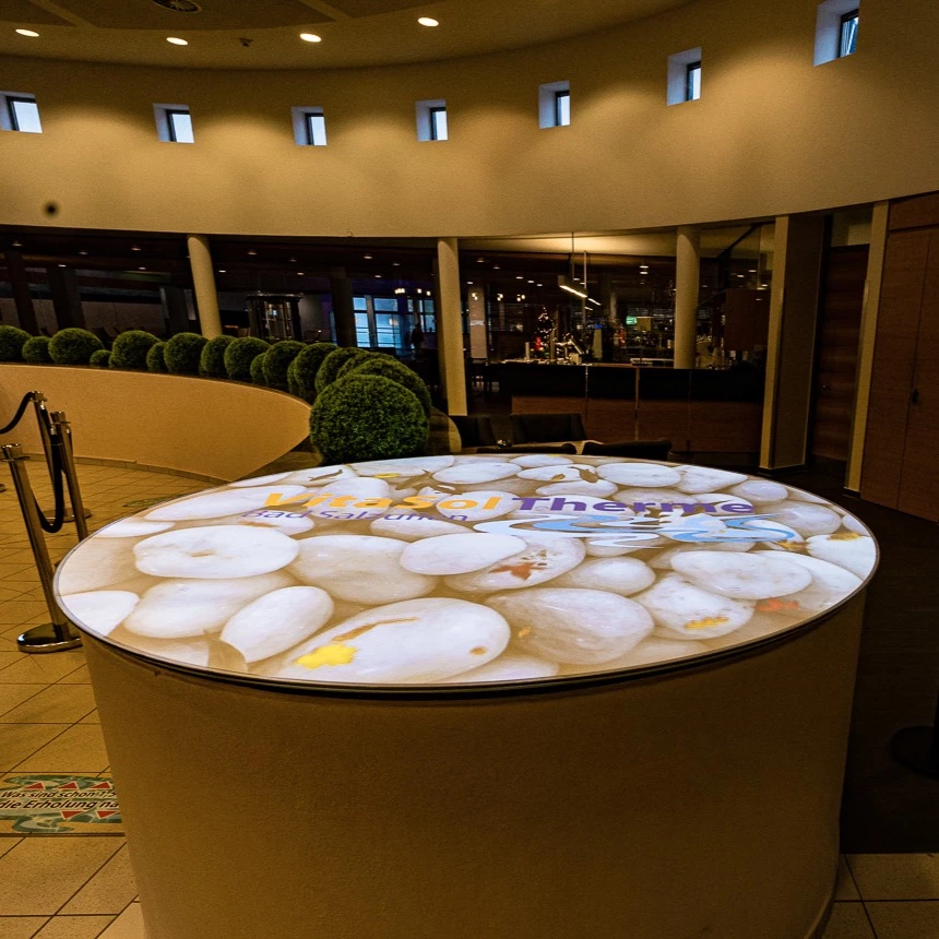 An interactive table projection in the foyer of the Therme VitaSol shows fish in the water in front of a stone underground
