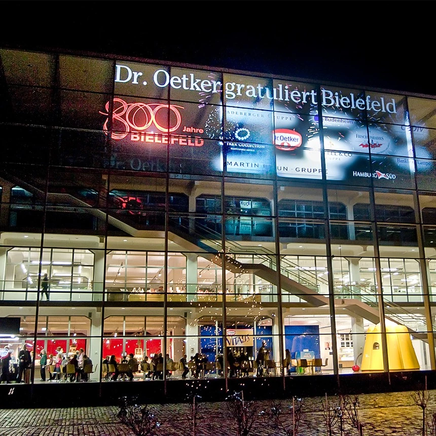 Rear projection on the glass facade by Dr. Oetker shows company logos and congratulations as an anniversary campaign