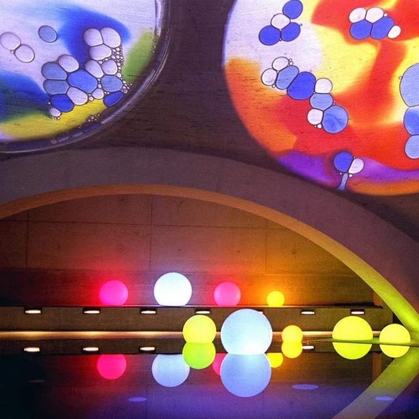 Colourful, luminous balls float on the water surface of a swimming pool, the ceiling is illuminated with atmospheric colors and shapes