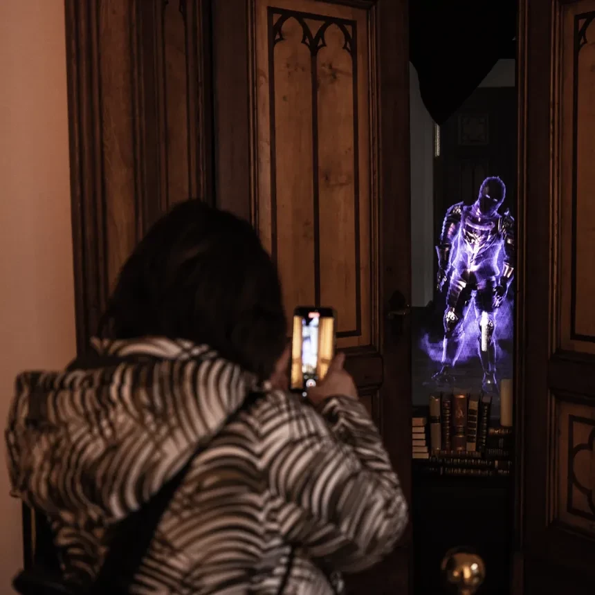 A woman films the hologram installation of a knight through a crack in the door with her smartphone