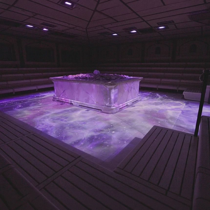 Immersive sauna experience at the Crystal Palace: Violet and white ambient projections on the floor and sauna heater create an atmospheric space of light—realized by TNL GmbH using 11 high-performance projectors in the world's largest immersive sauna.