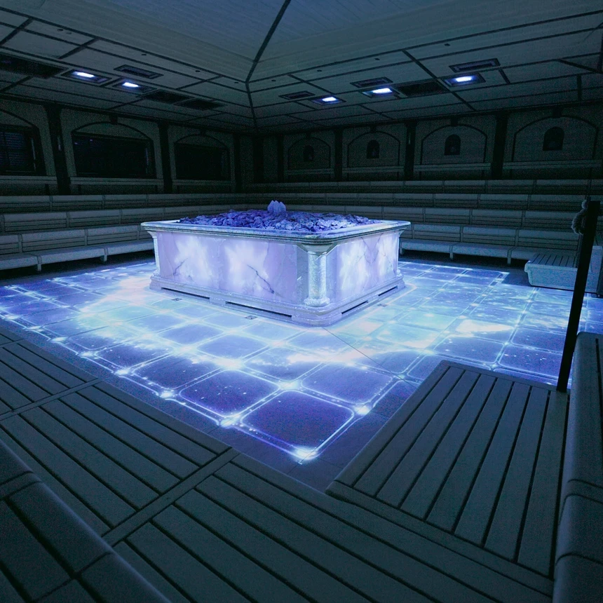 Crystal Palace Sauna with ice-blue floor projection: A glowing grid structure and points of light frame the central sauna heater—an immersive floor projection by TNL GmbH.