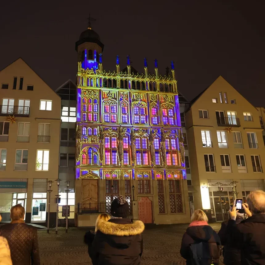 A projection mapping illuminates a facade in gold and neon colors