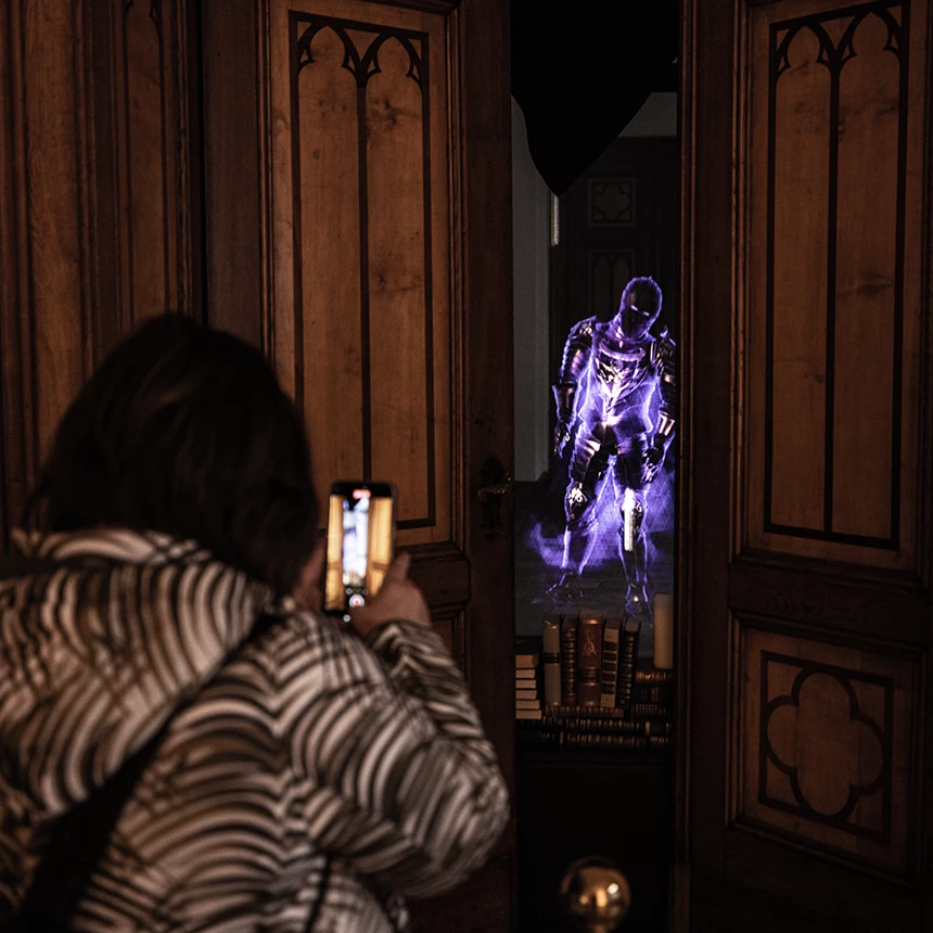 A woman photographs a hologram projection showing a knight through an open crack in the door