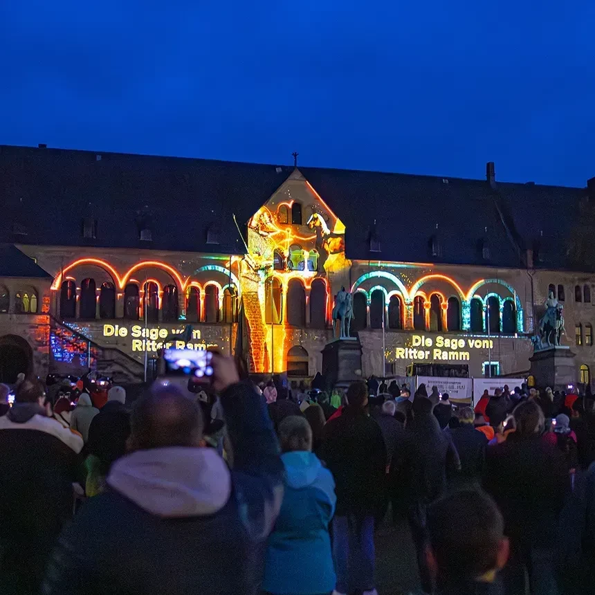 A crowd watches a projection mapping in which the window arches are outlined in bright colors