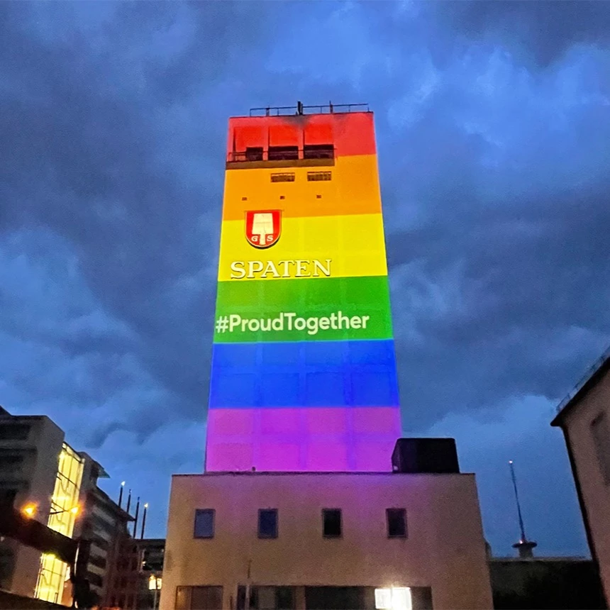 Tower illuminated with a rainbow flag in front of a night sky in Munich