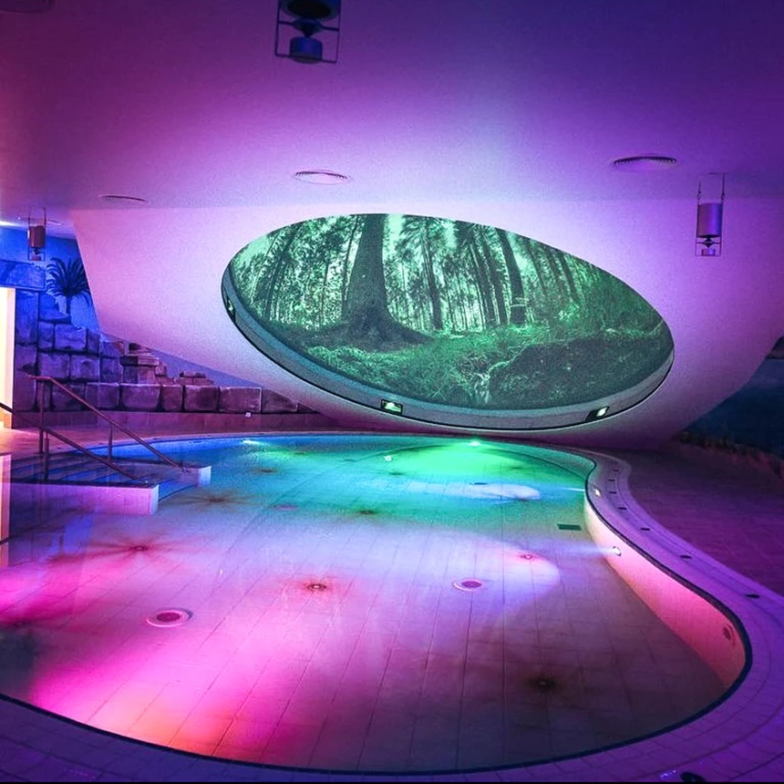 A small swimming pool is illuminated in moody purple, trees can be seen through an imaginary, projected window