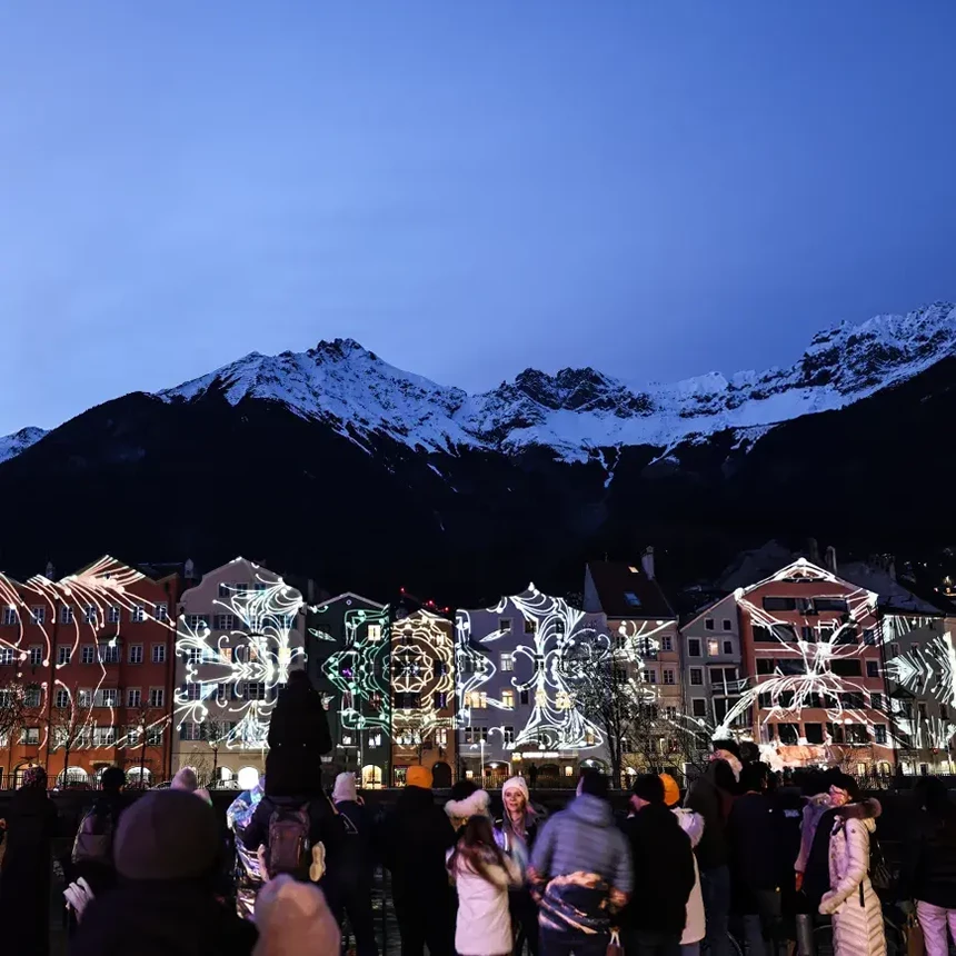 Menschen bestaunen das außergewöhnliche 3D-Videomapping auf der Mariahilf-Skyline mit Alpenpanorama im Hintergrund