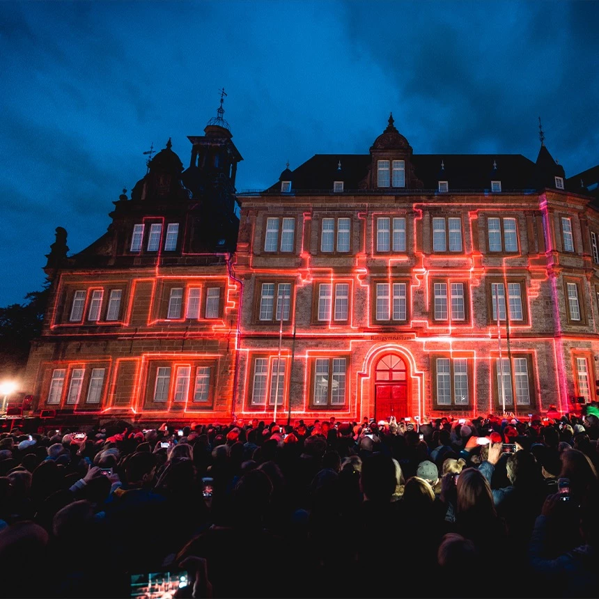 3D Video Mapping auf dem Bielefelder Ratsgymnasium bei dem mit roten Linien die Gebäudestrukturen nachgezeichnet werden