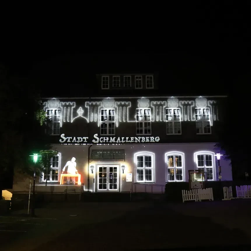 A small house is illuminated via projection mapping with the city name and white window borders