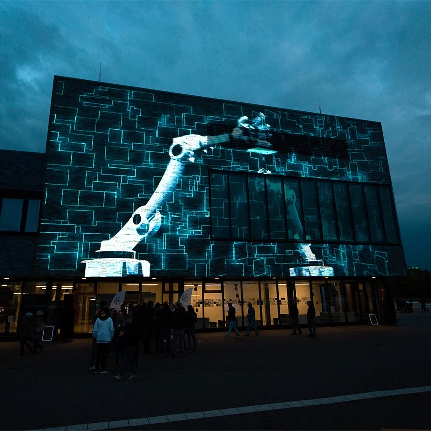 3D Video Mapping im technoiden Look zeigt Roboterarm auf Fassade von Hochschule Hamm-Lippstadt