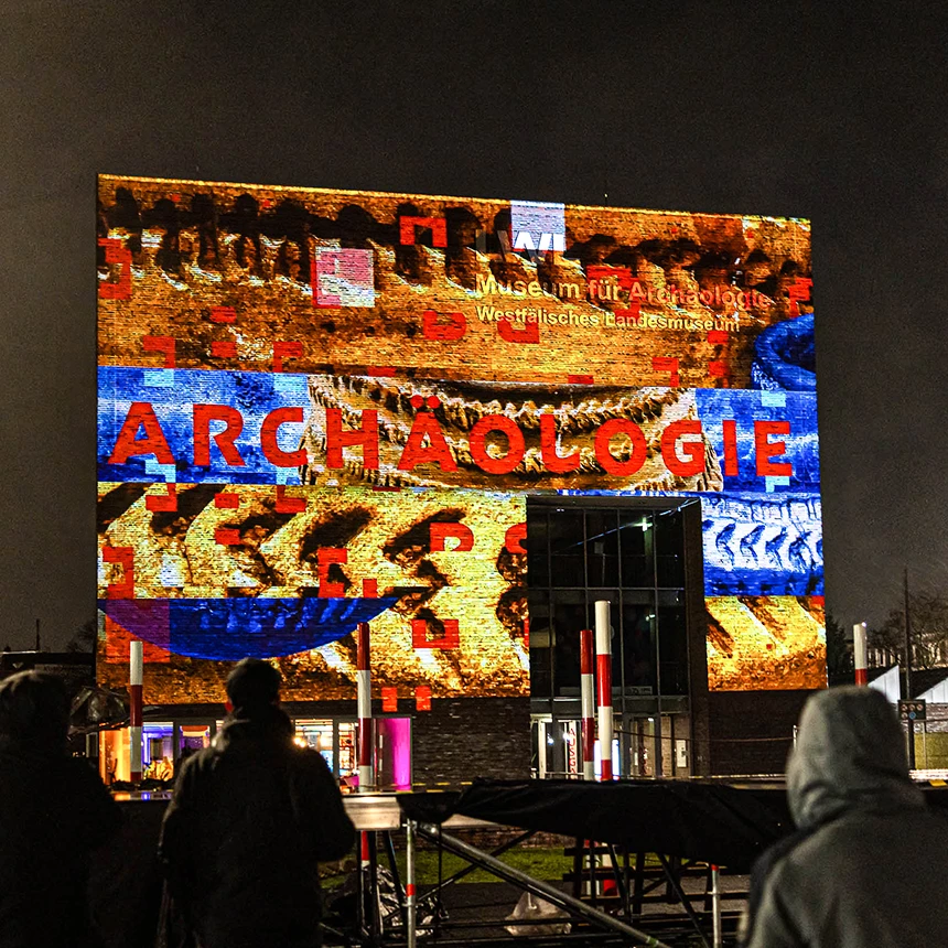 People look at a colorful video projection with the words Archeology at the LWL Museum in Herne