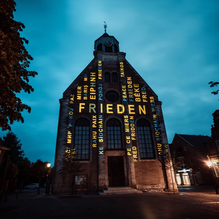 Light art installation on church with the word peace in different languages