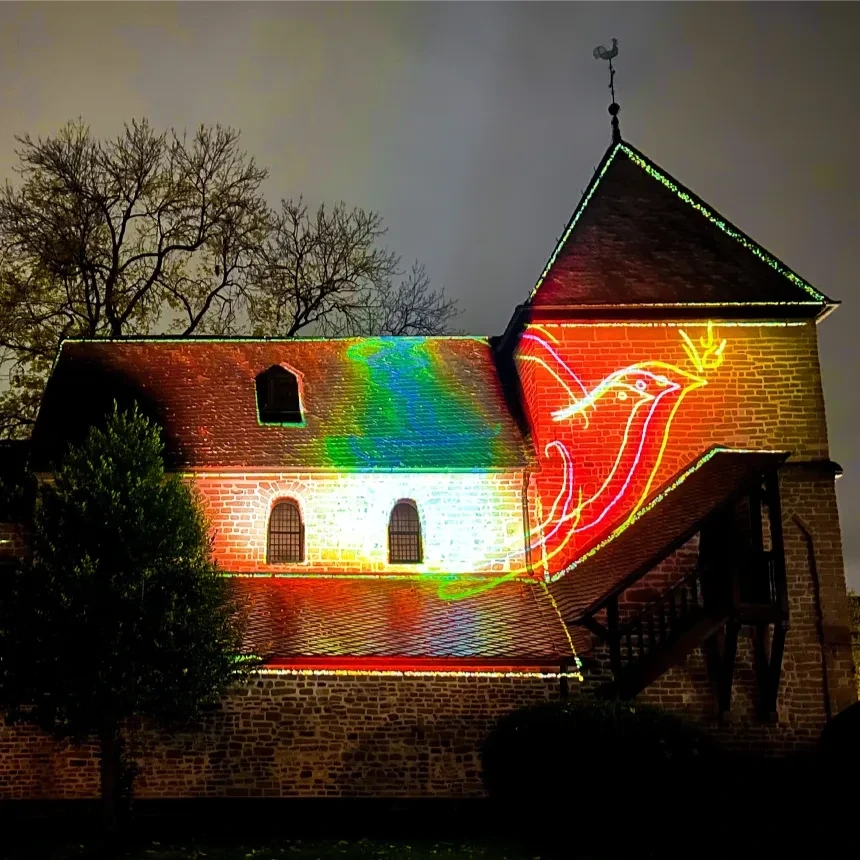 Small church with colorful light projection of a pigeon sketch by Pablo Picasso