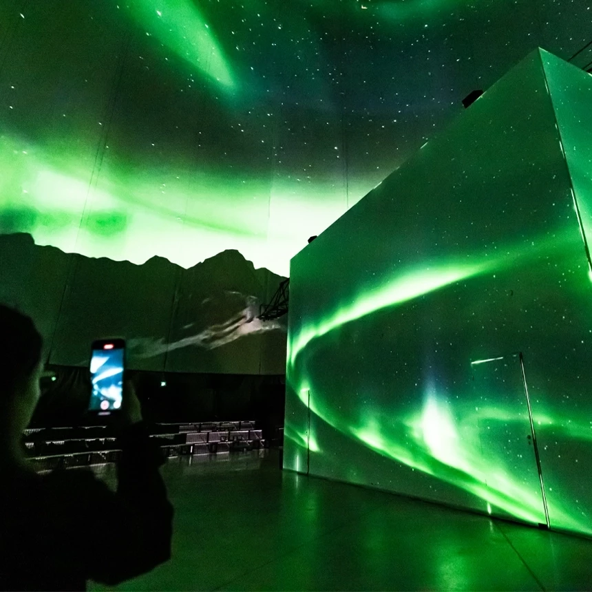 A person films the projection show in the Visiodrom with his mobile phone, which shows green northern lights.