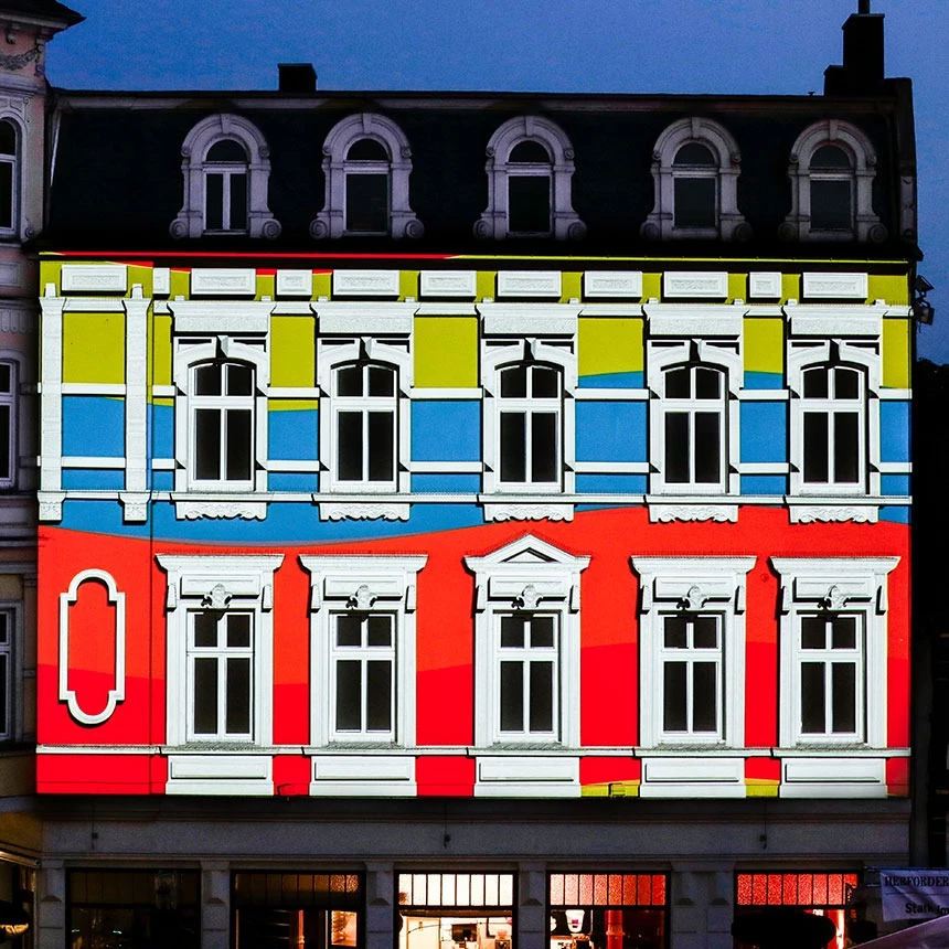 Die Fassade in neuem Gewand: mit Lichtprojektionen erscheint die gelbe Fassade nun in den Farben rot, blau und grün