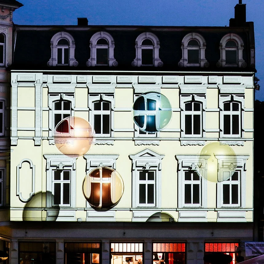 Als Effekt bei einer 3D Projektion fliegen überdimensionale Seifenblasen an einer Fassade virtuell in die Höhe