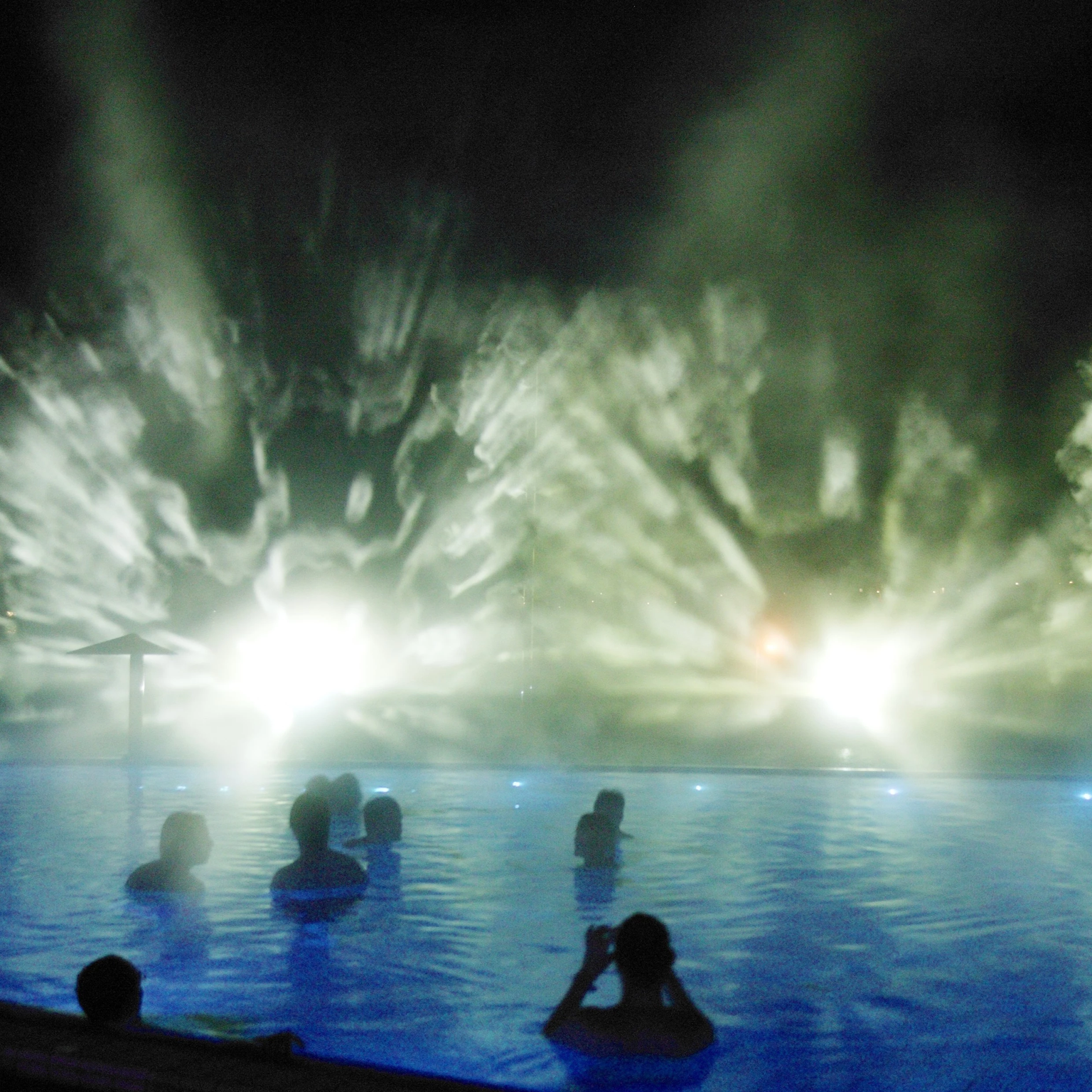 Visitors of the thermal baths look at the mystical fog projections while they are in the swimming pool of the outdoor area of Toskana Terme Bad Schandau