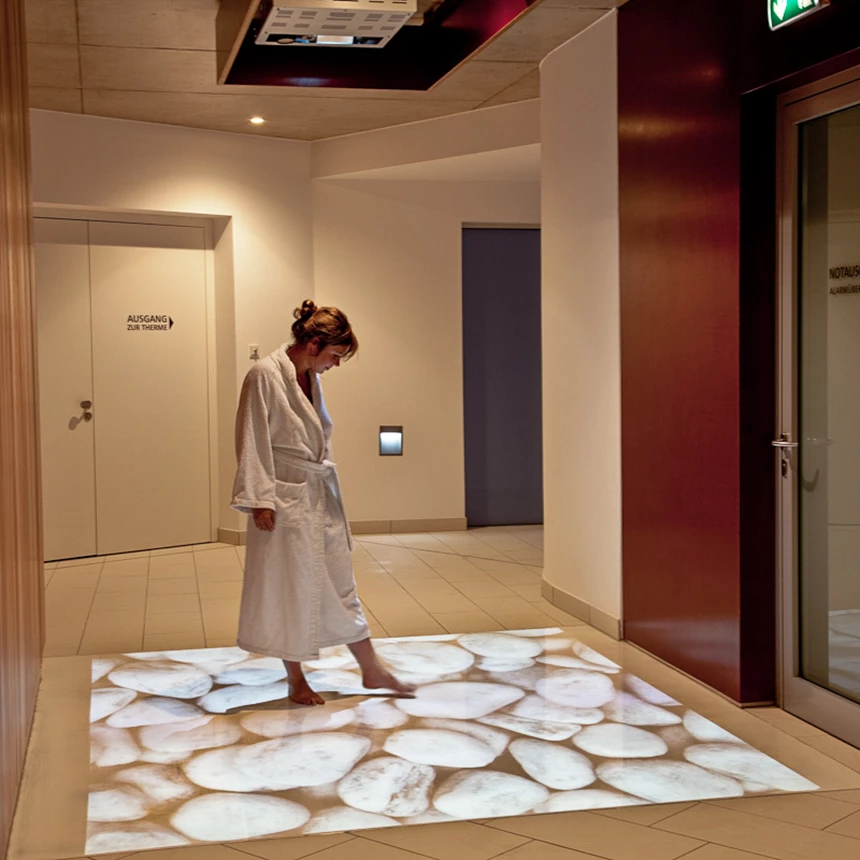 A woman stands on an interactive floor projection in the sauna area of a thermal bath