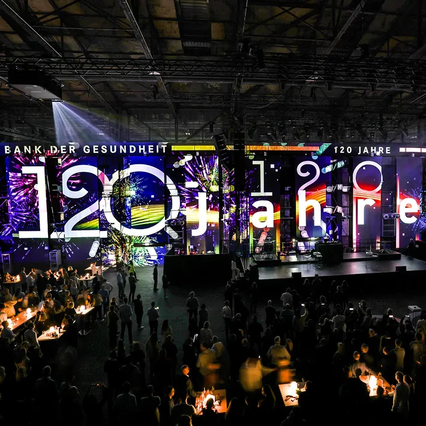 Guests at an apoBank incentive see a 3D video mapping with the words "120 years of the Health Bank" and digital fireworks in the background
