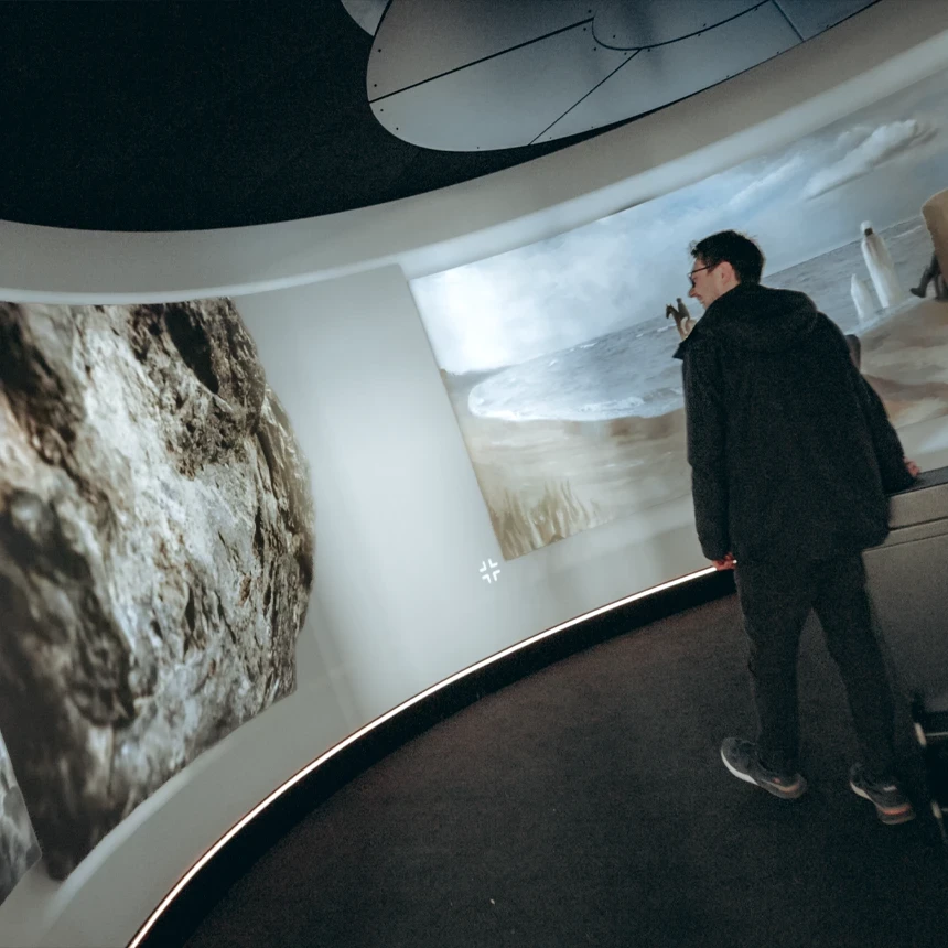 In the center of a round room with 360-degree projection, a person stands and looks at the various paintings on the concave wall.