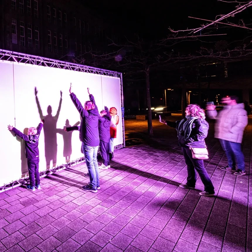 A family plays with light and shadow in front of a shadow wall