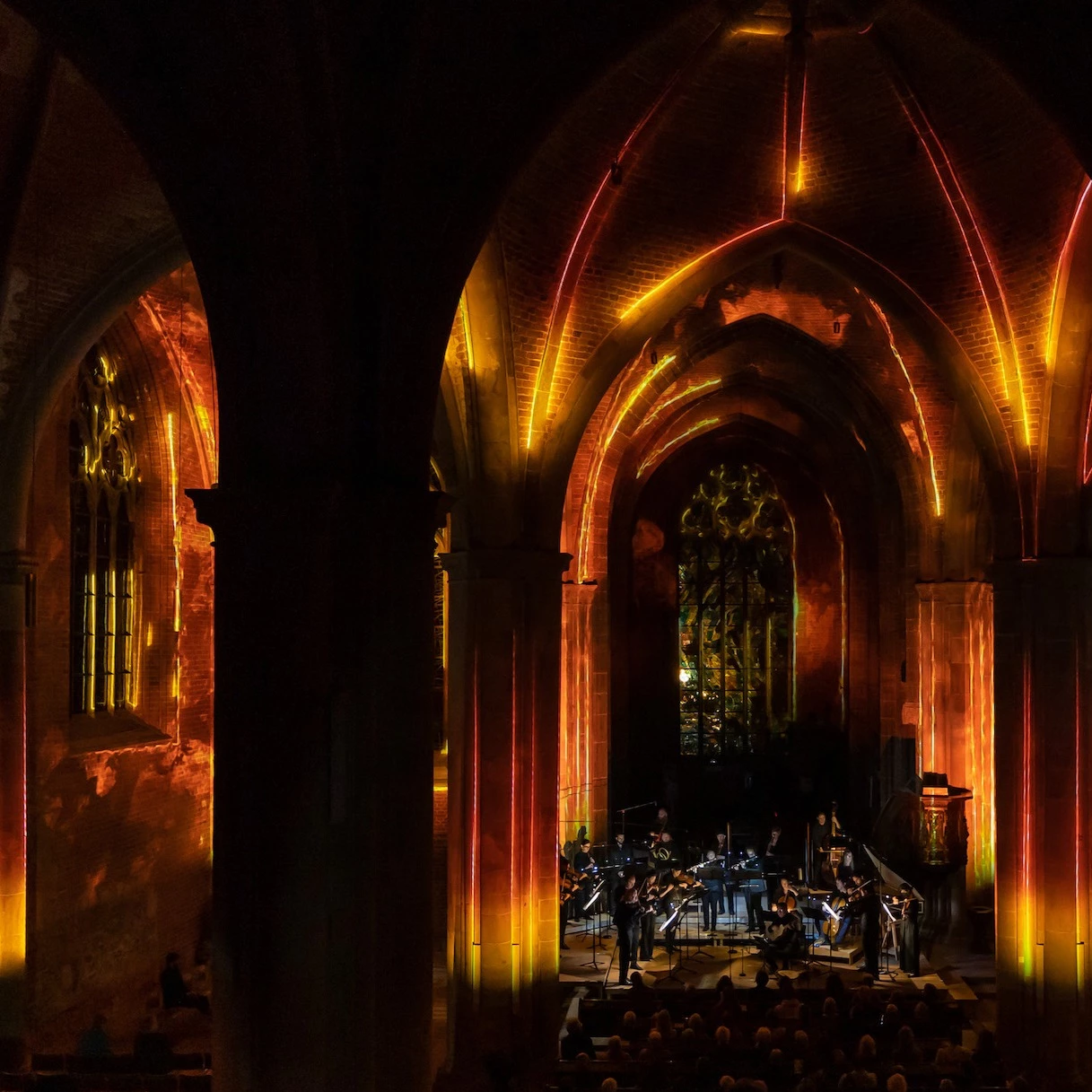 Projektionsshow in Kirche welche Raum und Klang aufgreift: das Orchester wird umgeben von Lichtkunst in orange