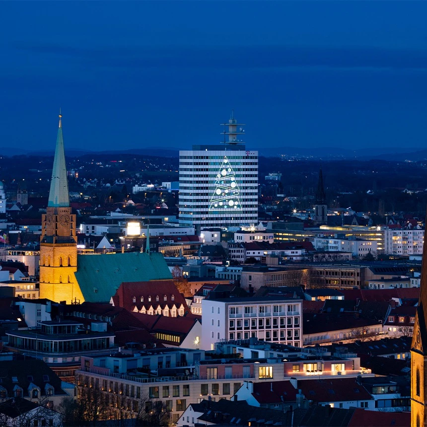 Stadtpanorama mit Großbild-Projektion auf Hochhaus-Fassade mit Logo der Stadt Bielefeld