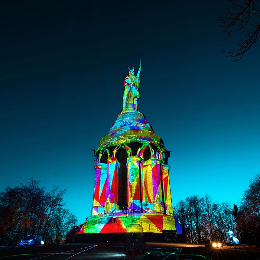 Hermannsdenkmal wird bei Abenddämmerung bunt beleuchtet