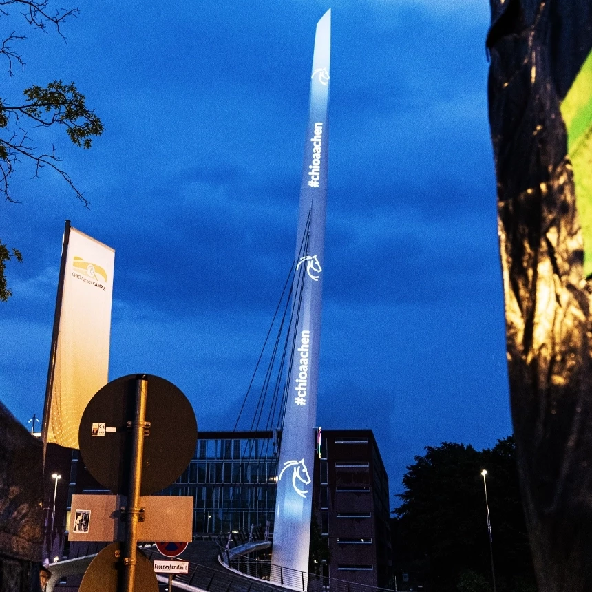 Auf der CHIO Nadel ist eine Projektion zu sehen, welche das Hashtag #chioaachen und das Logo der CHIO Aachen auf blauem Hintergrund zeigt