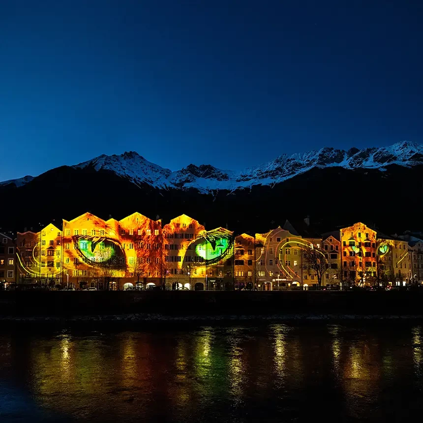 Video-Projektion von Wildkatzen-Augen auf die Skyline der Innsbrucker Mariahilf-Häuserzeile mit dem Inn im Vordergrund und Alpenpanorama im Hintergrund