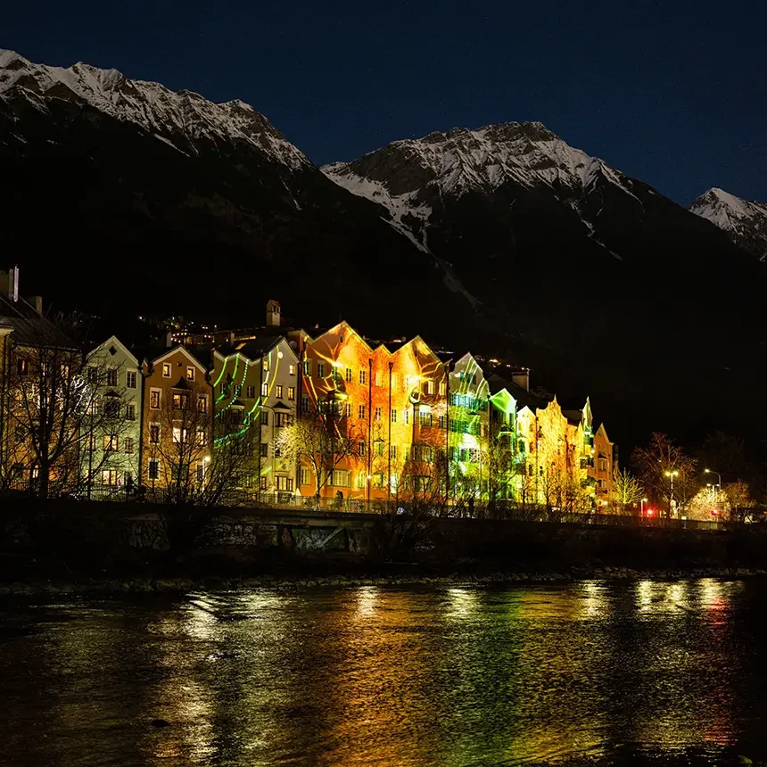 Die Innsbrucker Mariahilf-Häuserzeile mit dem Inn im Vordergrund und Alpenpanorama im Hintergrund als Station des Spaziergangs durch Licht: Inszenierung heimischer Tiere als Fassadenprojektion