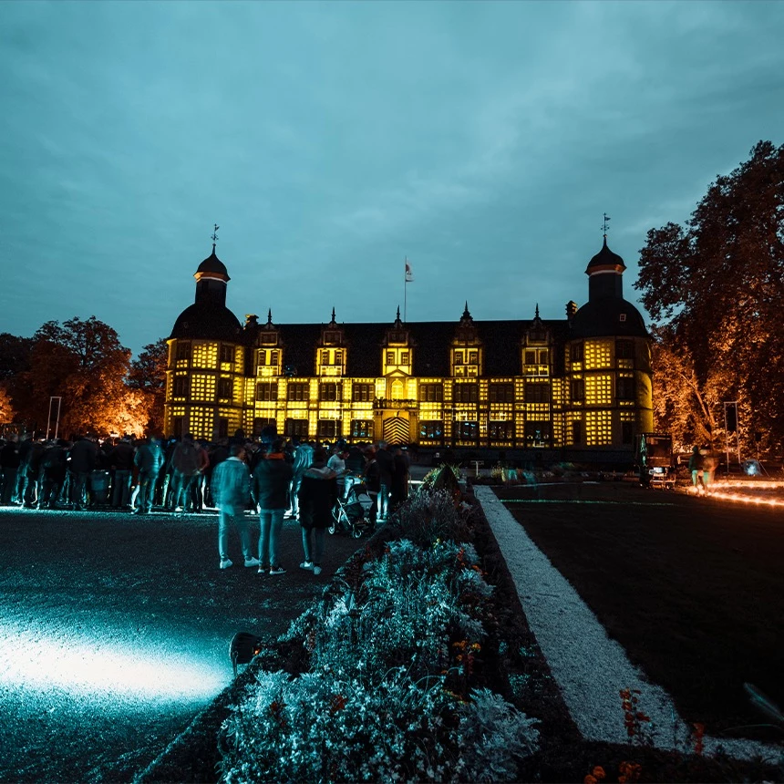 Fassadenprojektion mit Würfeln in 3D Optik auf Schloss Neuhaus mit Publikum im Vordergrund