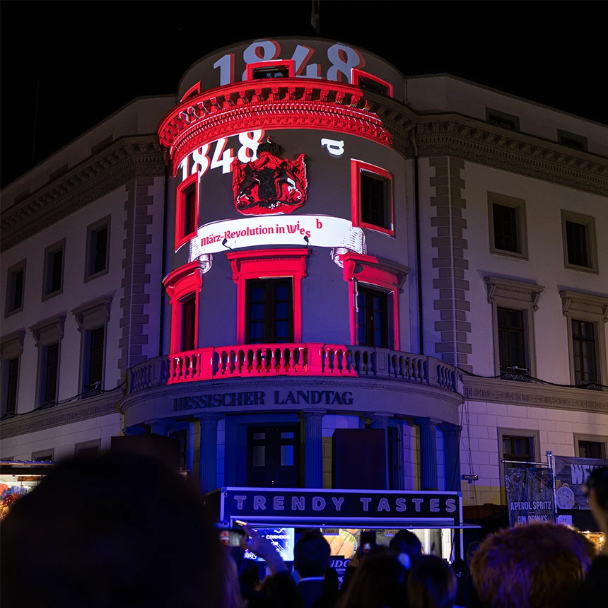 Die Fassade des hessischen Landtags wird rot und weiss, mit der Jahreszahl 1848 angestrahlt. Die Fassadenprojektion deutet auf „März-Revolution in Wiesbaden“ hin.
